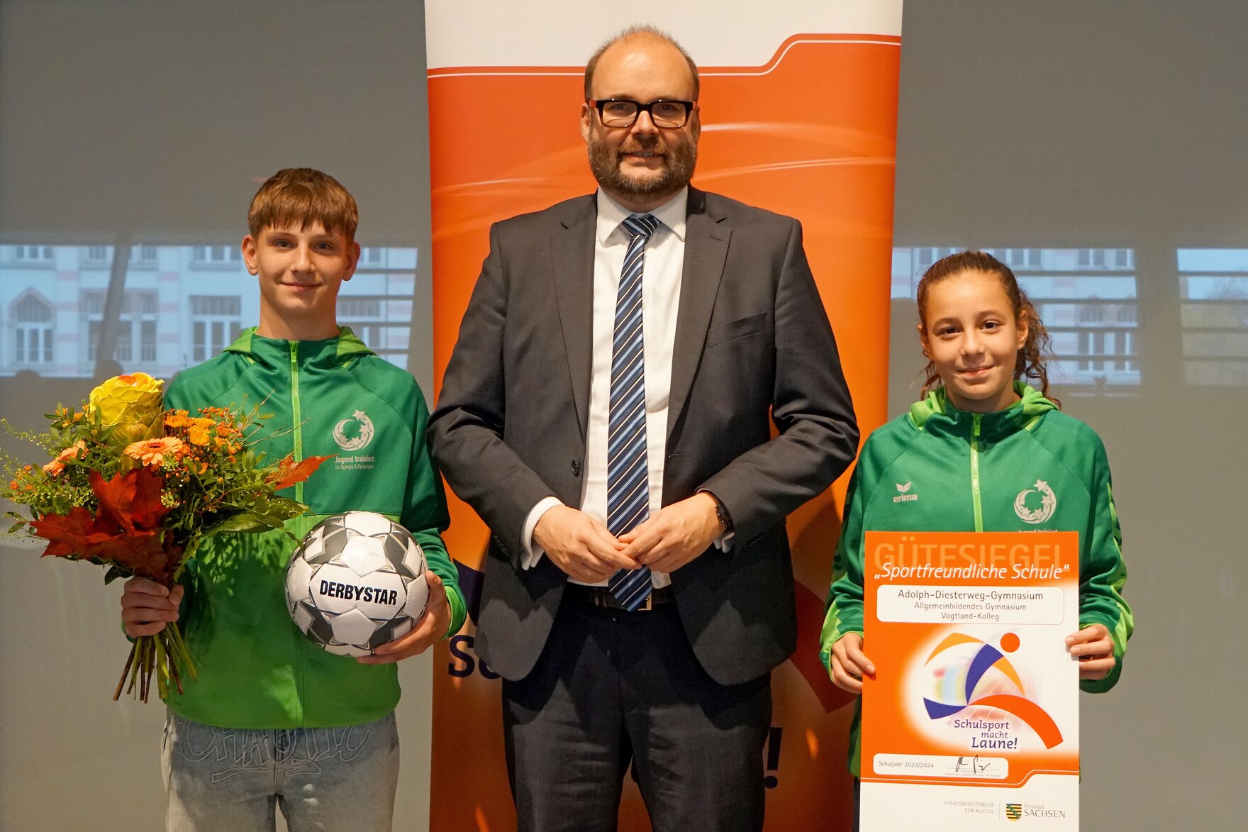 Kultusminister in der Mitte Schüler links mit Ball - Schülerin mit Urkunde